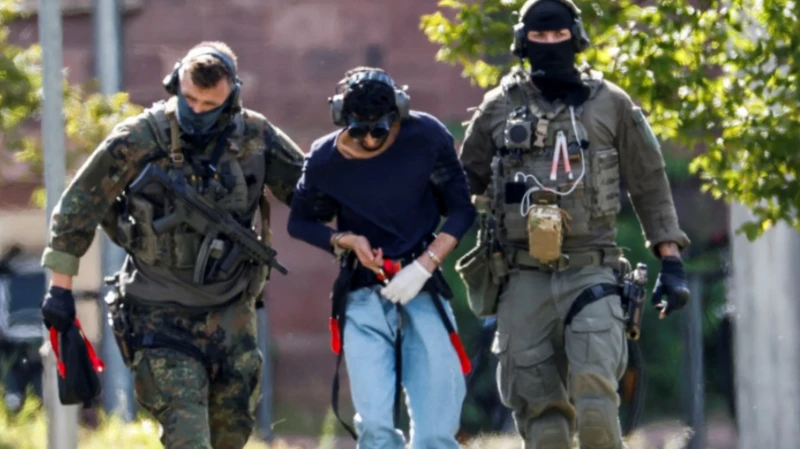 El sospechoso del ataque escoltado por dos policías este domingo.